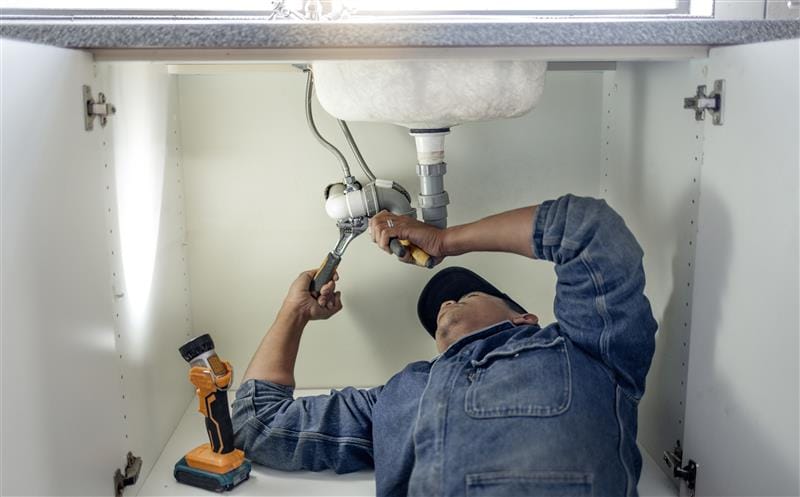 Plumber repairing pipes beneath a bathroom sink in Duarte